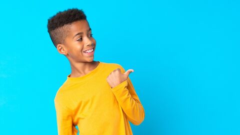 Guck mal nach da! Junge in gelbem Shirt steht vor blauer Wand und zeigt lachend nach rechts