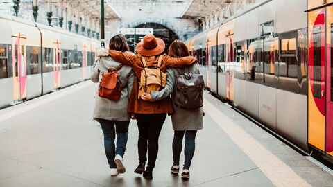 Freunde am Bahngleis Drei Freunde sieht man von hinten wie sie Arm in Arm neben den Zügen am Bahngleis entlang laufen.